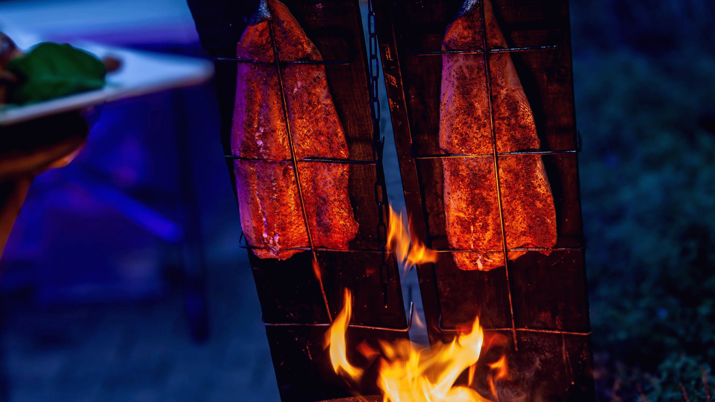 Twee planken met zalm staan schuin bij het open vuur