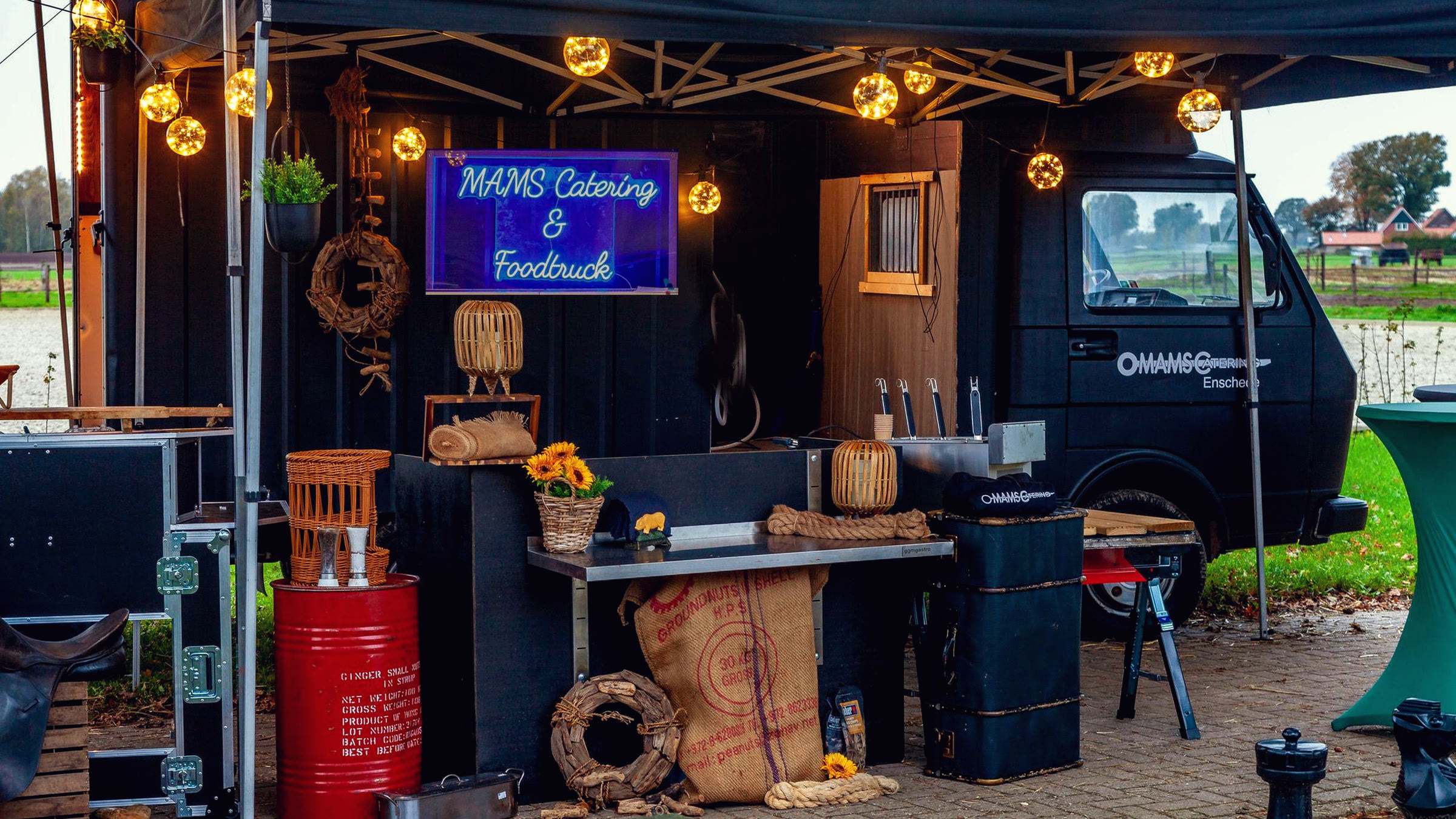 De foodtruck van MAMS bij schemer met lichtsnoeren en neonbord