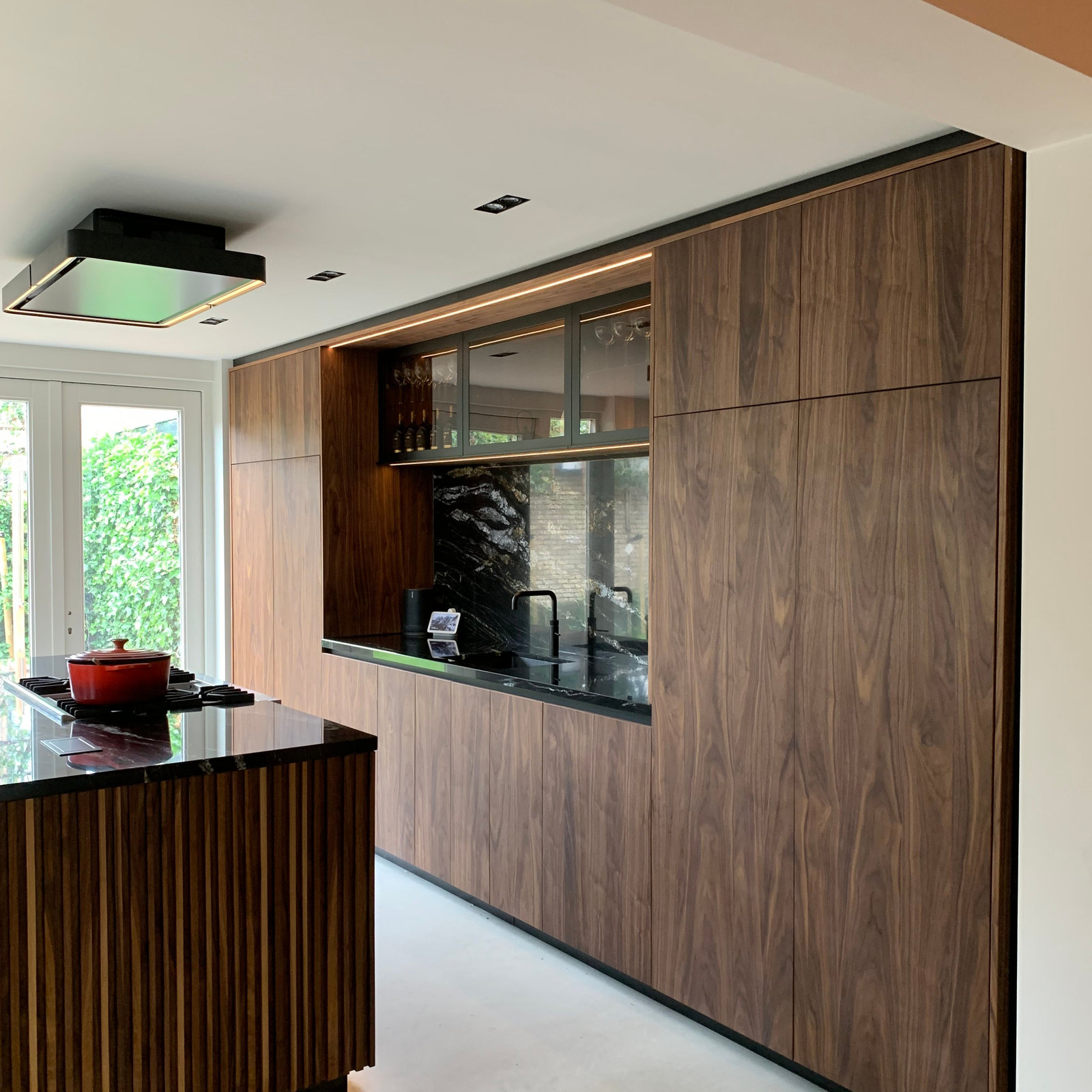 Hoge notenhouten kastenwand in een keuken met doorkijk naar de tuin